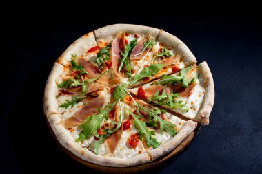 Pizza with jamon or prosciutto, mozzarella, cherry tomatoes, arugula and parmesan on a black background. Italian cuisine