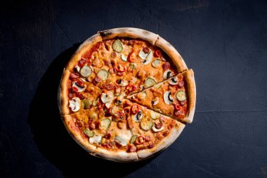 Appetizing pizza with hunting sausages, mozzarella cheese, pickled cucumbers, chili peppers on a tomato base. Mexican pizza. Top view.