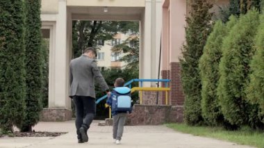 Baba oğlunu elinden tutar ve çocuğu okula götürür, uğurlar ve elveda der, dost canlısı aile..