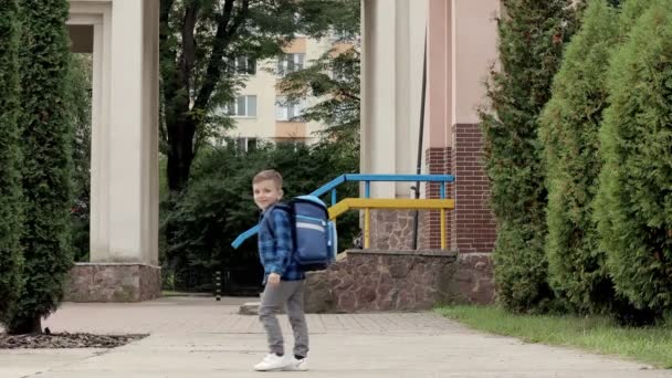 リュックを持った男の子が手を振って学校に行く 後ろの景色 一年生 — ストック動画