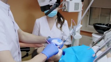 Mikroskop altında asistanı olan dişçi hastanın dişlerini tedavi ediyor. Modern ilerici dişçilik.