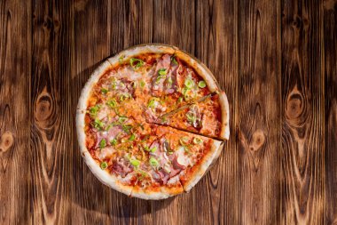 Delicious pizza with mozzarella cheese, ham, leeks on a tomato base on wood background.