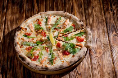 Pizza with salmon, mozzarella, cherry tomatoes, arugula, lemon and parmesan. Italian cuisine on a woden background.