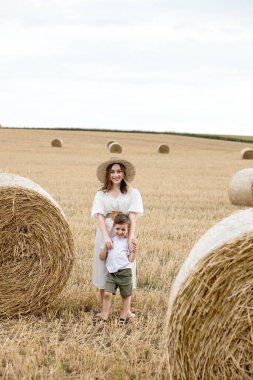 Genç anne ve oğul saman yığınlarının yanında yürüyor. Hasat sonrası saman yığınları, hasat edilen ekinlerle dolu tarlalar..