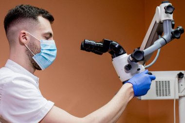 Erkek bir dişçi mikroskoba bakar. Yeni teknolojiler kullanan modern dişçilik.