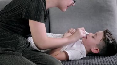Anne oğluna burun ve burun damlaları püskürtüyor. Çocuk için burun spreyi kullanan bir kadın. Burun akışı, soğuk algınlığı, grip, hastalık, virüs