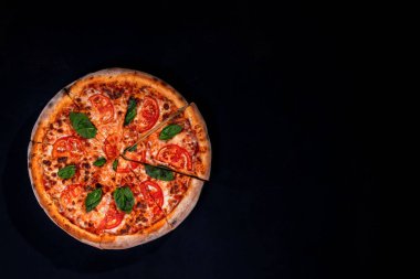 Delicious fragrant pizza-Margherita with mozzarella, tomatoes and basil on tomato sauce on black background. Copy space.