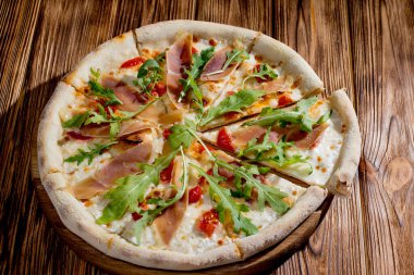 Pizza with jamon and prosciutto, mozzarella, cherry tomatoes, arugula and parmesan on a wood background. Italian cuisine