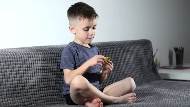 一个小男孩坐在舒适的沙发上 打开糖果 嘴里衔着番石榴 小孩子喜欢吃糖果 — 图库视频影像