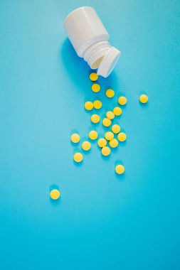 Sarı ilaç, mavi arka planda şişesi olan haplar. Metin için alanı kopyala.