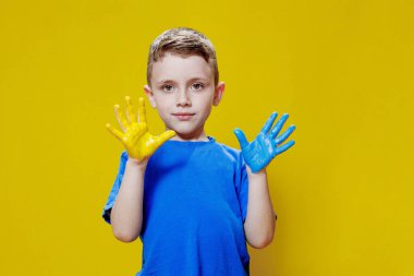 Avuç içleri sarı ve maviye boyanmış, Ukrayna bayrağı renginde küçük mutlu bir çocuk. Ukraynalı yaratıcı anaokulu öğrencisi.