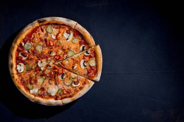 Appetizing pizza with hunting sausages, mozzarella cheese, pickled cucumbers, chili peppers on a tomato base on black background.