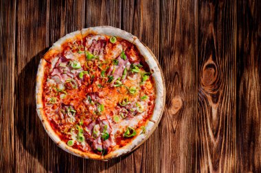 Delicious pizza with mozzarella cheese, ham, leeks on a tomato base on wood background.