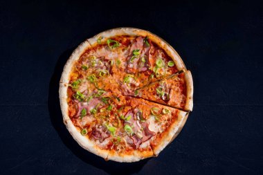 Delicious pizza with mozzarella cheese, ham, leeks on a tomato base on black background.
