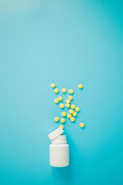 Sarı ilaç, mavi arka planda şişesi olan haplar. Metin için alanı kopyala.