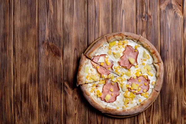 Delicious pizza with ham, pineapple, corn on a creamy base on woden background. Hawaiian pizza.