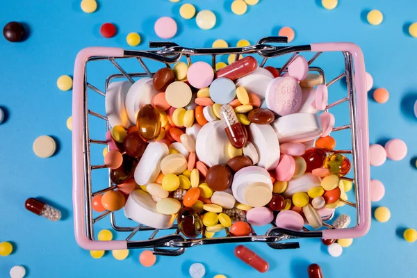 Various capsules, pills and medicines in a shopping cart on a blue background. Health care, treatment. The concept of buying pills and buying medicine.