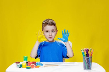 Küçük bir anaokulu öğrencisi masada oturuyor, avuç içlerini bir kağıt parçasına çiziyor. Renkli el izleri. Anaokulu geliştirme.