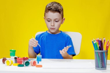 Küçük bir anaokulu öğrencisi elinde fırçayla masada oturur ve avucunu boyar. Anaokulu geliştirme