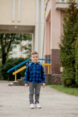 Sırt çantası ve ders kitaplarıyla mavi gömlekli okul çocuğunun portresi. Küçük okul çocuğu. Birinci sınıf öğrencisi.