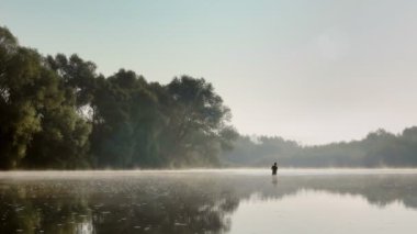 Sisli bir yaz sabahı nehirde balık tutan bir balıkçı. Döndürmek için balık tutmak