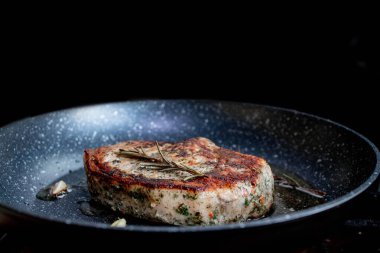 Grilled premium rib eye beef steak in the pan, cooking steak in the kitchen on a dark background. Overhead shot of chef preparing ribeye with butter, thyme and garlic