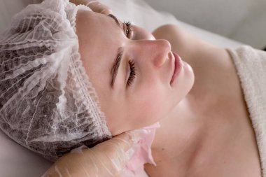 Kozmetik prosedürü. Genç bir kadının yüzü. Kadın bir kozmetikçinin elleri beyaz bir kadının yüzünü ve boynunu ıslak mendille siliyor. Gençleştirir ve rahatlatır.