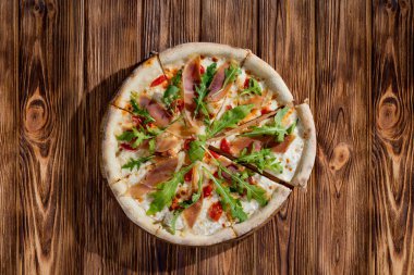 Pizza with jamon and prosciutto, mozzarella, cherry tomatoes, arugula and parmesan on a wood background. Italian cuisine