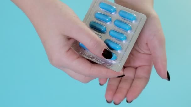 ブリスターパックから青いカプセル薬を取り出す女性の手のクローズアップ 青い背景で — ストック動画
