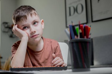Boy sitting at the table, studying mathematics, got tired and leaned on his hand