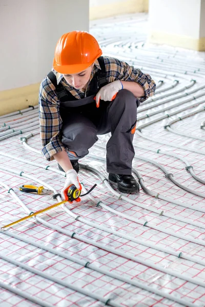 A female construction worker checks the installation of a warm floor with a tape measure at the construction site