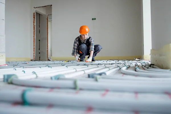 A female construction worker checks the installation of a warm floor with a tape measure at the construction site