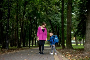 Genç bir kadın güneşli bir günde heyecanlı oğlunu birinci sınıfa götürüyor. Çalışmaya hazır.
