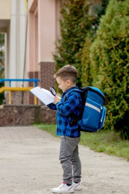 Küçük bir okul çocuğu ders kitabına büyüteçle bakıyor. Küçük çocuklar için eğitim. Okul konseptine dönelim..