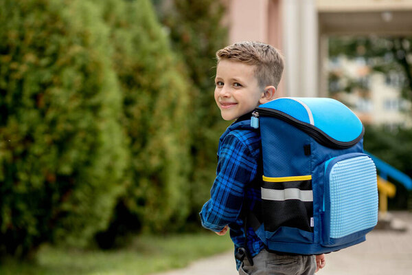 Little first grader with a blue backpack goes to school.