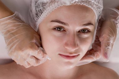 Kozmetik prosedürü. Genç bir kadının yüzü. Kadın bir kozmetikçinin elleri beyaz bir kadının yüzünü ve boynunu ıslak mendille siliyor. Gençleştirir ve rahatlatır.