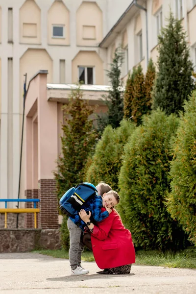 幼い母親は学校に行く途中で興奮した一級の息子を抱きしめる 勉強の準備 — ストック写真