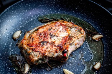 Grilled premium rib eye beef steak in the pan, cooking steak in the kitchen on a dark background. Overhead shot of chef preparing ribeye with butter, thyme and garlic