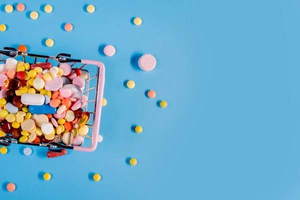 Various capsules, pills and medicines in a shopping cart on a blue background. Health care, treatment. The concept of buying pills and buying medicine.