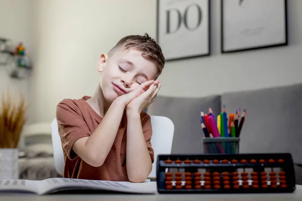 テーブルに座って数学を勉強している男の子は疲れて手にもたれて目を閉じた — ストック写真