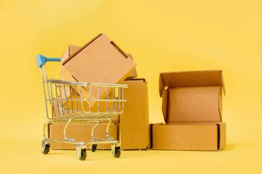 Sarı arka planda kutuları olan alışveriş arabası. Satış, indirim, online alışveriş ve teslimat kavramı.