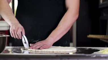 Profesyonel bir mutfakta aşçı yuvarlak hamurun kenarlarını budarmış. Pizza için hazırlıklar.