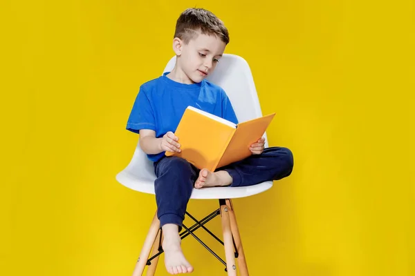 少し陽気なブロンドの緑目の男の子5 6歳でスタイリッシュな青のTシャツを保持本と黄色の壁の背景に読書 子供のスタジオの肖像画 — ストック写真