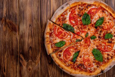 Delicious fragrant pizza-Margherita with mozzarella, tomatoes and basil on tomato sauce on woden background. Copy space.