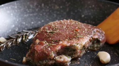 Meat steak is fried in rosemary oil and garlic in a frying pan.