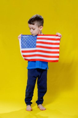 Sarı arka planda Amerikan bayrağı tutan gülümseyen küçük çocuk. Vatanseverlik, bağımsızlık günü, bayrak günü konsepti. Anma Günü.