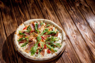 Pizza with jamon and prosciutto, mozzarella, cherry tomatoes, arugula and parmesan on a wood background. Italian cuisine