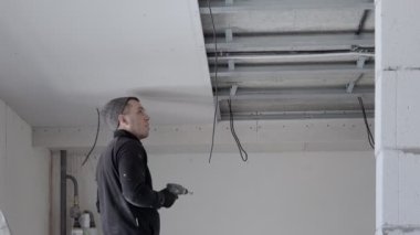 İnşaat işçisi asılmış tavanı alçıpanla birleştiriyor ve alçıpanı tornavidayla tavandaki metal çerçeveye yerleştiriyor. Tadilat, inşaat ve kendin yap.