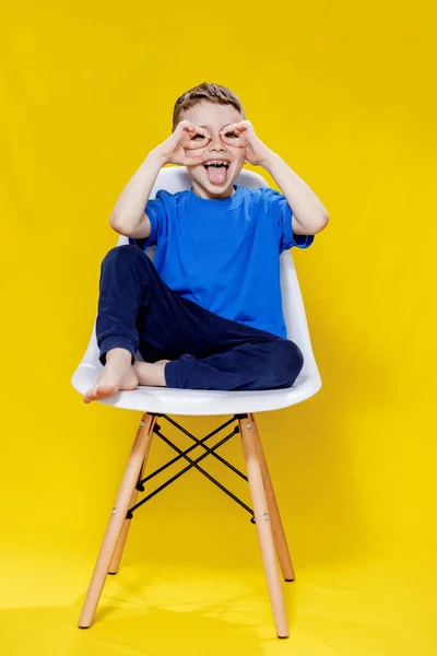 黄色の椅子に座って陽気な小さな男の子 明るく遊び心のある肖像画 — ストック写真