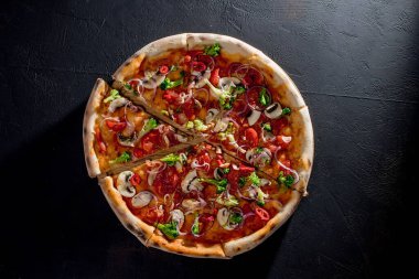 Vegan pizza with tomato sauce, cherry tomatoes, mushrooms, broccoli, red onion on black background. View from above.